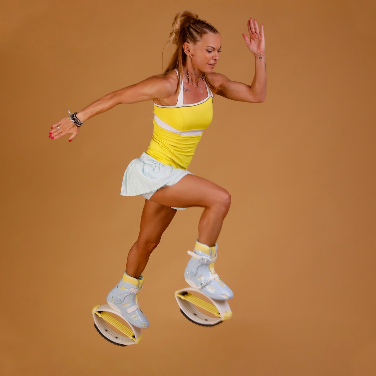 Femme sautant en portant des Fit Boots Rebound Boots bleues et jaunes