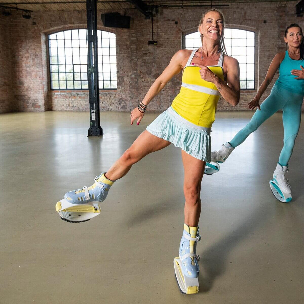 Dos mujeres hacen ejercicio en interiores con unas botas de rebote azules y amarillas Fit Boots